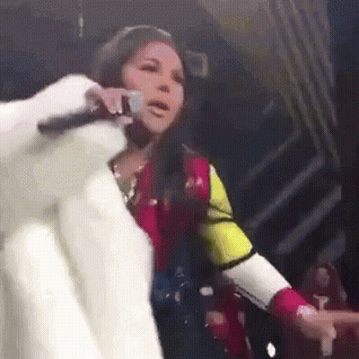A Woman In A Fur Coat Is Singing Into A Microphone GIF