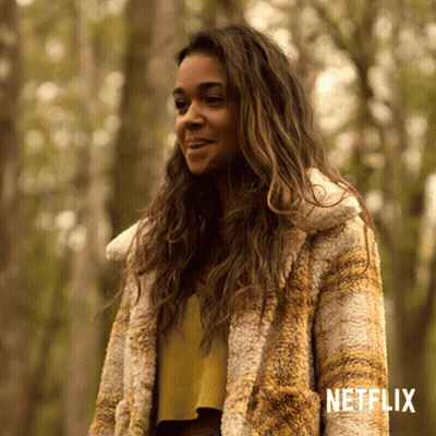 A Woman In A Fur Coat Is Standing In A Forest With Netflix Written On The Bottom GIF