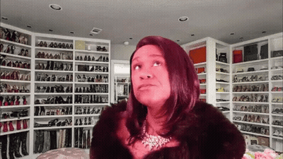 A Woman In A Fur Coat Is Standing In Front Of A Wall Of Shoes GIF