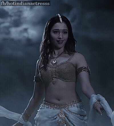 A Woman In A Gold Bra And White Pants Is Dancing In The Dark . GIF
