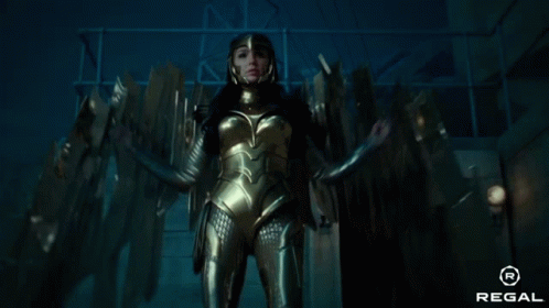 A Woman In A Gold Costume Is Standing In A Dark Room With A Regal Logo In The Corner GIF