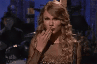 A Woman In A Gold Dress Is Blowing A Kiss . GIF