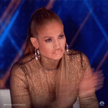 A Woman In A Gold Dress Is Clapping Her Hands While Wearing Hoop Earrings . GIF