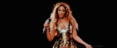 A Woman In A Gold Dress Is Singing Into A Microphone On A Stage In Front Of A Black Background . GIF