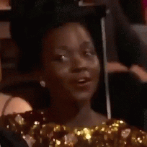 A Woman In A Gold Dress Is Sitting In A Chair And Making A Face . GIF