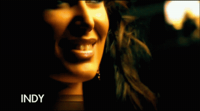 A Woman In A Gold Dress Is Standing In A Room With The Word Indy On The Bottom Left GIF