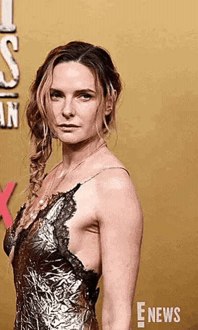 A Woman In A Gold Dress Is Standing On A Red Carpet And Looking At The Camera . GIF