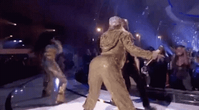 A Woman In A Gold Jumpsuit Is Dancing On A Stage In Front Of A Crowd . GIF