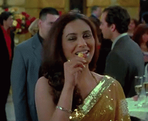 A Woman In A Gold Sequined Dress Is Eating A Piece Of Food GIF