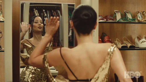 A Woman In A Gold Sequined Dress Looks At Herself In A Mirror With Hbo Written On The Bottom GIF