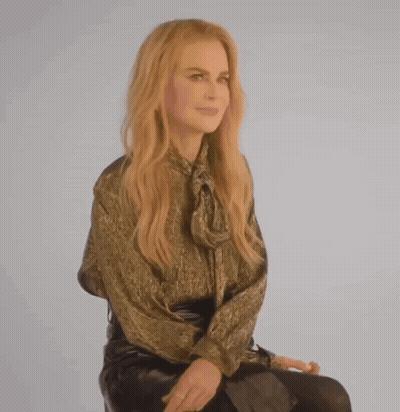 A Woman In A Gold Shirt And Black Skirt Is Sitting On A Chair GIF