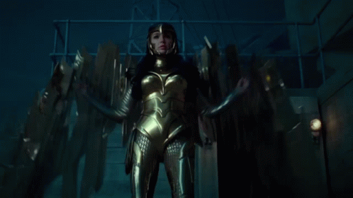 A Woman In A Gold Suit And Helmet Is Standing In A Dark Room GIF
