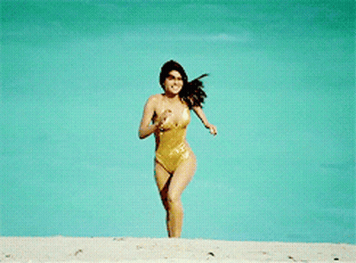 A Woman In A Gold Swimsuit Is Running On A Beach GIF