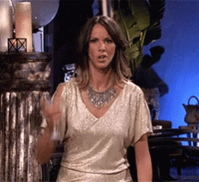 A Woman In A Gold Top And Silver Necklace Holds A Glass GIF
