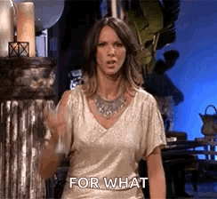 A Woman In A Gold Top Is Standing In Front Of A Metal Pillar And Says `` For What '' . GIF