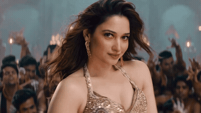 A Woman In A Gold Top Stands In Front Of A Crowd Of People GIF