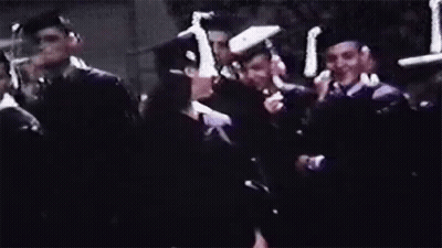 A Woman In A Graduation Cap And Gown Is Smiling In Front Of A Crowd Of People . GIF