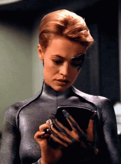 A Woman In A Gray Bodysuit Is Holding A Pen GIF