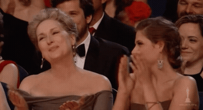 A Woman In A Gray Dress Is Applauding Another Woman GIF