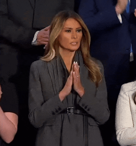 A Woman In A Gray Jacket Is Praying With Her Hands Together GIF