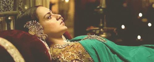 A Woman In A Green And Gold Dress Is Laying Down GIF