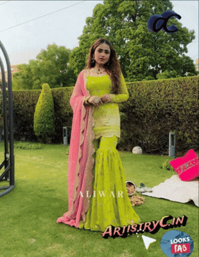 A Woman In A Green And Pink Dress Is Standing On A Lush Green Lawn GIF