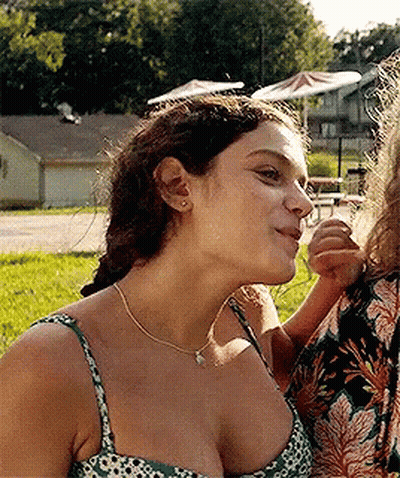 A Woman In A Green And White Floral Tank Top Looks Down At Something GIF