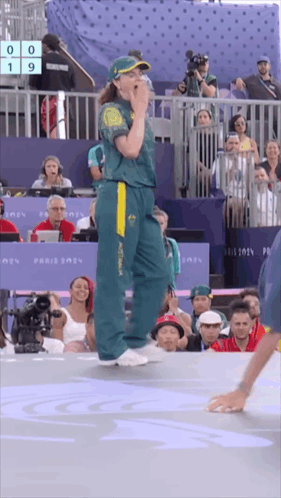A Woman In A Green And Yellow Australia Jersey Stands In Front Of A Crowd GIF