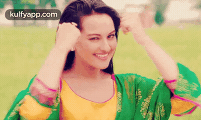 A Woman In A Green And Yellow Dress Is Smiling While Holding Her Hair . GIF
