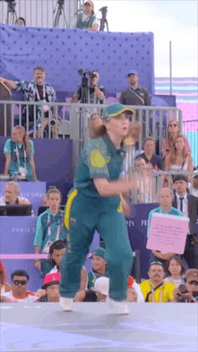 A Woman In A Green And Yellow Outfit Is Dancing In Front Of A Crowd Of People GIF