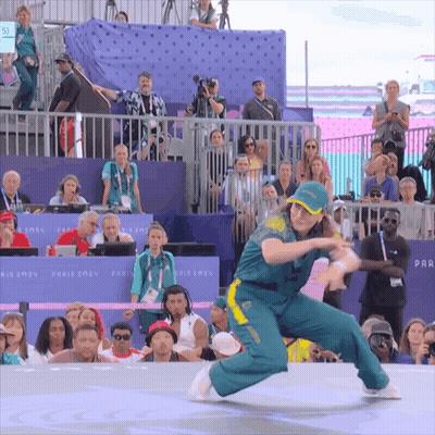 A Woman In A Green And Yellow Outfit Is Dancing In Front Of A Crowd That Is Watching GIF
