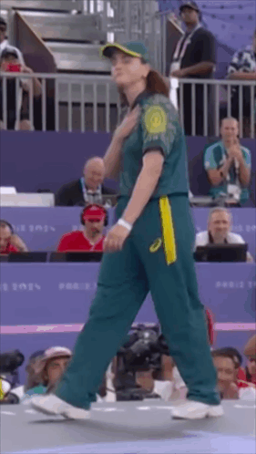 A Woman In A Green And Yellow Uniform Is Walking In Front Of A Crowd . GIF
