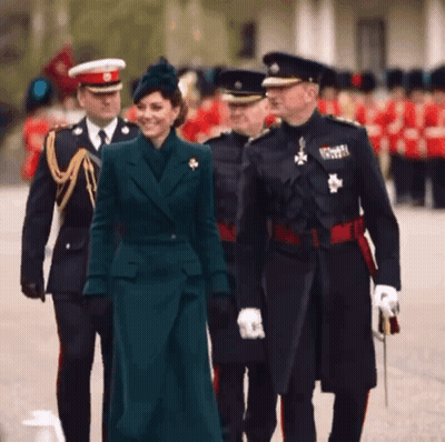 A Woman In A Green Coat Is Walking With A Group Of Men In Uniforms GIF
