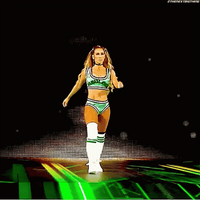 A Woman In A Green Crop Top And Shorts Is Walking On A Stage . GIF