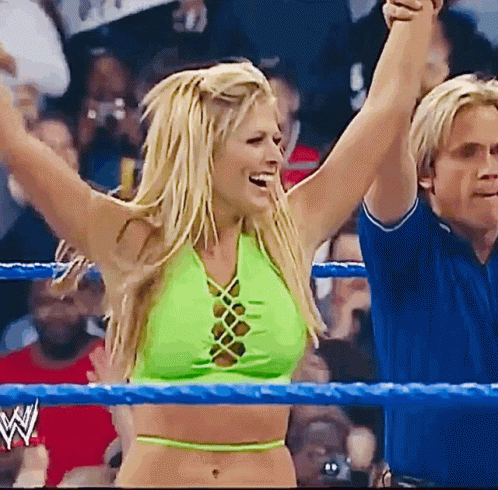 A Woman In A Green Crop Top Stands In A Wrestling Ring With Her Arms In The Air GIF