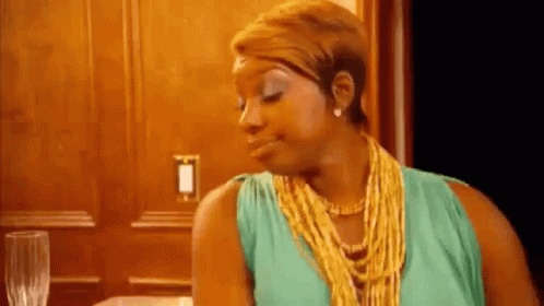 A Woman In A Green Dress And A Gold Necklace Is Sitting At A Table . GIF