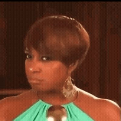 A Woman In A Green Dress And Earrings Is Making A Face . GIF