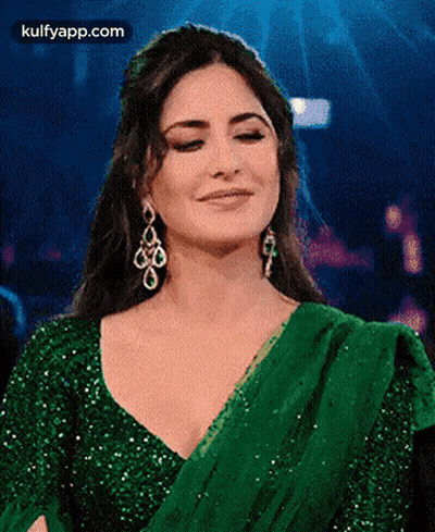 A Woman In A Green Dress And Earrings Is Smiling . GIF