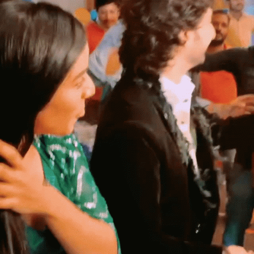 A Woman In A Green Dress Is Being Hugged By A Man In A Black Suit GIF