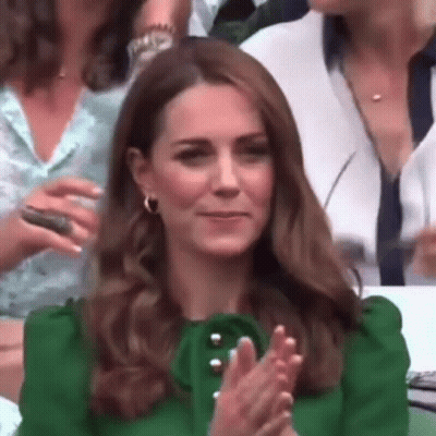 A Woman In A Green Dress Is Clapping Her Hands In A Crowd Of People . GIF
