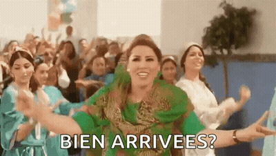 A Woman In A Green Dress Is Dancing In Front Of A Crowd With The Words Bien Arrivees ? Written Below Her . GIF