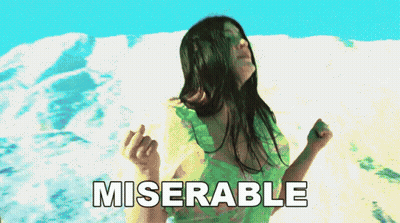 A Woman In A Green Dress Is Dancing In Front Of A Snowy Mountain And The Word Miserable Is Written Below Her GIF
