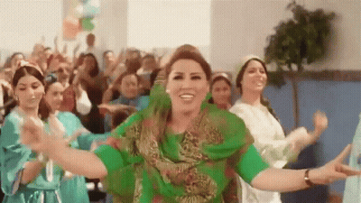 A Woman In A Green Dress Is Dancing With A Group Of Women In Blue Dresses . GIF
