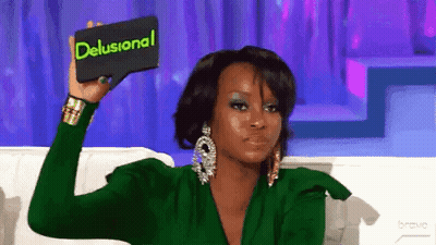 A Woman In A Green Dress Is Holding A Card That Says Delusional GIF