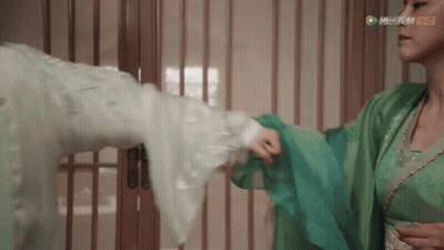 A Woman In A Green Dress Is Holding A Man 'S Arm In A Room GIF