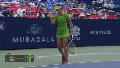 A Woman In A Green Dress Is Holding A Tennis Racquet In Front Of A Mubadala Advertisement GIF