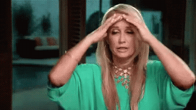 A Woman In A Green Dress Is Holding Her Head In Pain . GIF