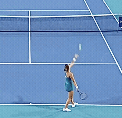 A Woman In A Green Dress Is Playing Tennis On A Court GIF