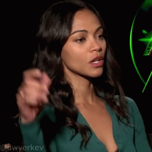 A Woman In A Green Dress Is Pointing Her Finger At Something . GIF