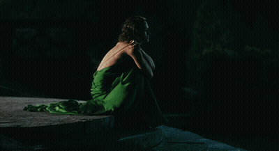 A Woman In A Green Dress Is Sitting On A Rock In The Dark GIF